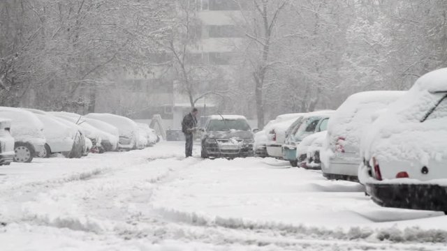 Man Cleaning His Car Of Snow In A Full Parking Lot, Blizzard, Winter, Cars