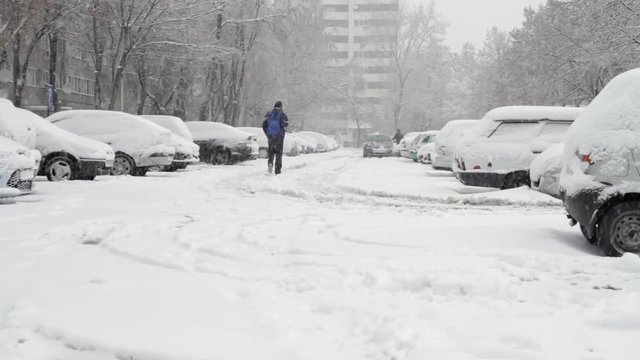 Young Man Walking In A Parking Lot Covered In Snow, Blizzard, Winter, Tilt Down