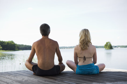 A man and a woman sitting on a bridge with their legs crossed, rear view.