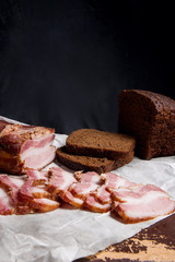 Puff smoked bacon with rye black bread on the packaging paper. V