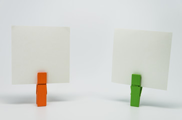 Piece of Memo paper clamped by orange and green wooden clip with white background and selective focus