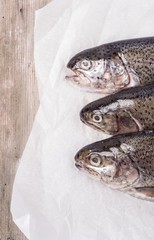 Three raw trouts on paper with thyme and lemon on a rustic wooden table
