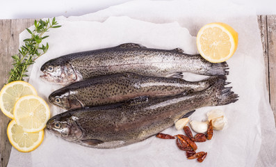Three raw trouts on paper with thyme and lemon on a rustic wooden table