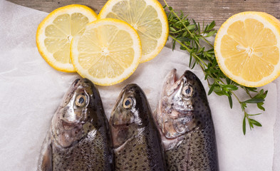 Three raw trouts on paper with thyme and lemon on a rustic wooden table