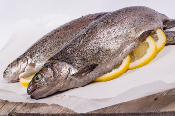 Three raw trouts on paper with thyme and lemon on a rustic wooden table