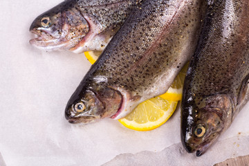 Three raw trouts on paper with thyme and lemon on a rustic wooden table