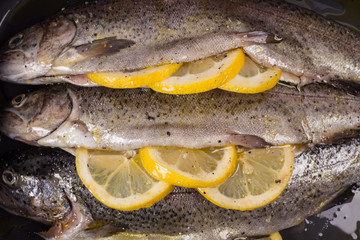 Three raw trouts on paper with thyme and lemon on a rustic wooden table