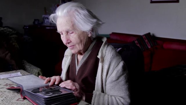 99 Years Old Woman Sitting At Table And Flipping Through An Old Photo Album, Pan