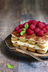 Homemade tiramisu with raspberry on a black plate.