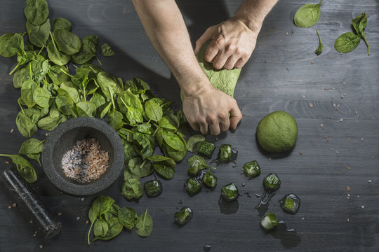 Cropped image of hands kneading green dough by basil ice cubes at table