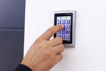 Man dialing pass code on intercom security keypad to open entrance door of the apartment building.