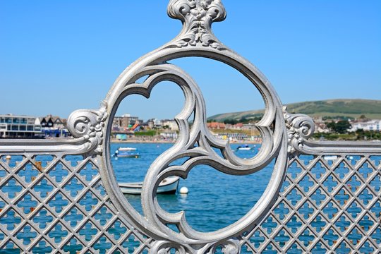 Victorian decorative iron railings along the pier with the town to the rear, Swanage.