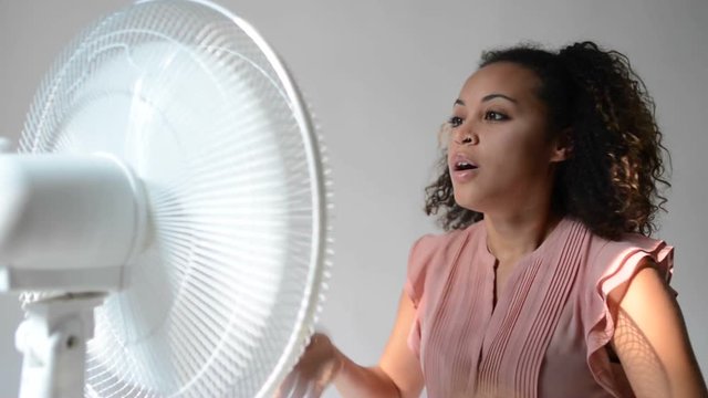 Black woman feeling hot and sitting in front of an electric fan to get some cool air on her face