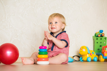 Fototapeta na wymiar 1,5 year-old child playing with educational cup toys at home. Little blond baby boy with blue eyes is playing with pyramid toy on the floor. Little kid have fun indoors