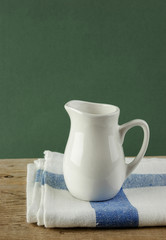 White jug and dishcloth on old wooden table over green backgroun