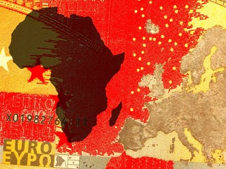 The African policy of Europe -
A European map in golden colors is right of the African continent in black. Background: red.
