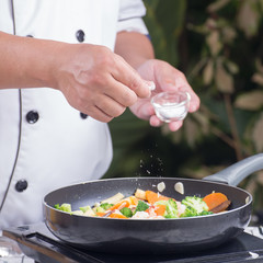 Chef putting Salt to the pan for cooking vegetable