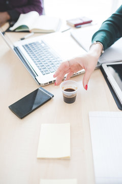 Close up on the hand of businesswoman holding a cup of coffee on a desk with technological devices - business, break, working concept