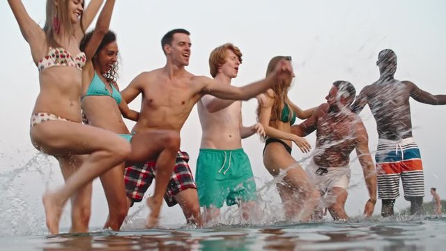 Group of young friends full of happiness dancing in the water and splashing it