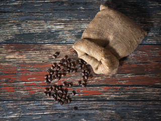 Sack of coffee and spilled coffee beans on old wooden boards
