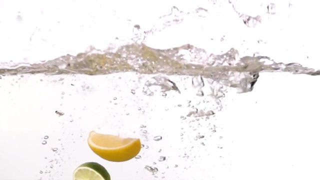 Sliced lime and lemon falling into water on white background slow motion HD video. Water surface with floating citrus fruits, splash bubbles and waves.