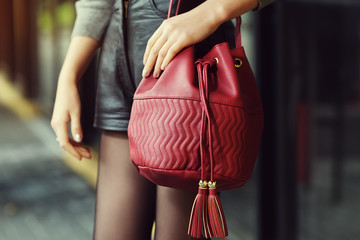 Elegant outfit. Closeup of red leather bag in hands of stylish woman. Fashionable girl on the...