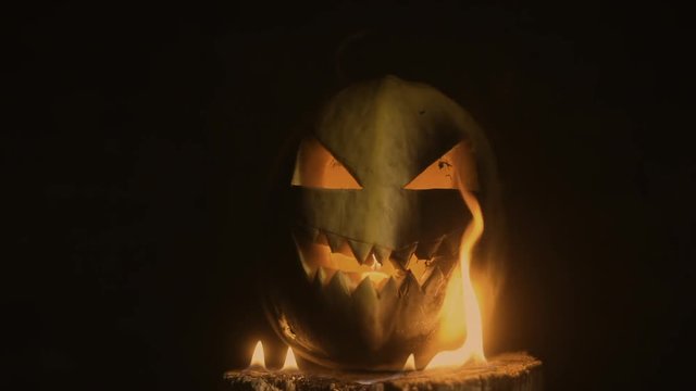 Scary carved halloween pumpkin in hot burning hell fire flames. The big helloween pumpkin has a mad face with glowing eyes and also a glow in its mouth and teeth.