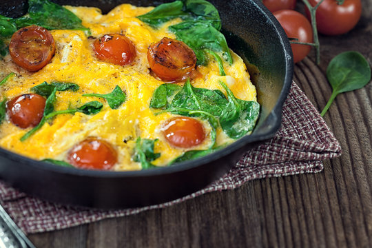 Spinach frittata with cherry tomato in iron skillet 