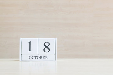 Closeup surface white wooden calendar with black 18 october word on blurred brown wood desk and wood wall textured background with copy space , view another more date in my portfolio