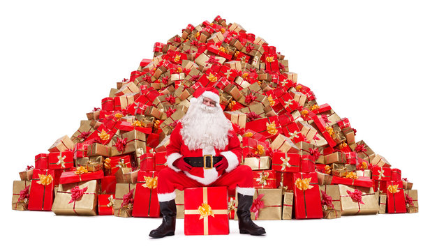 Santa Claus sitting in front of a pile of Christmas gifts isolated on white background