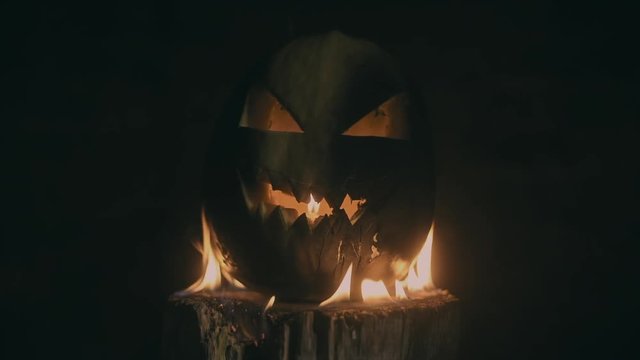 Scary carved halloween pumpkin in hot burning hell fire flames. The big helloween pumpkin has a mad face with glowing eyes and also a glow in its mouth and teeth.