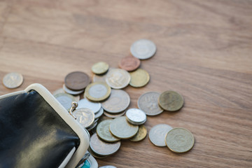 Black leather wallet with different coins on the wooden surface