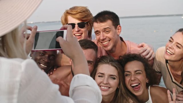 Woman taking picture of her friends grimacing and making hilarious faces at the camera on the beach