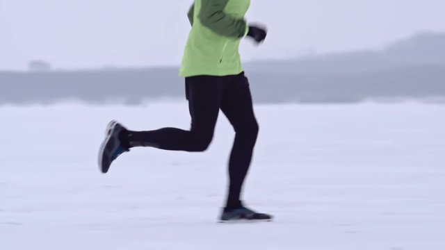 Tracking shot of young man running in snow while preparing for winter marathon