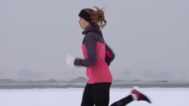 Tracking shot of fit woman running in snowy countryside on cold winter day
