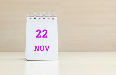 Closeup surface note book with purple 22 nov word in page on blurred brown wood desk and wood wall textured background with copy space under window light