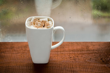 Large cup of coffee with marshmallows on the window in the rain.