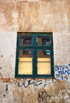 Old decayed flaking painted wood window fastened in a dirty plastered wall with grafitti tags, on a townhouse in Elsinore, Denmark