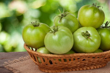 unripe green tomatoes in a wicker basket on  wooden table with  blurred background