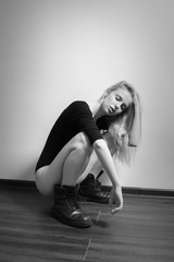 Fototapeta na wymiar sad blond girl in black male boots sitting squat on floor, monochrome