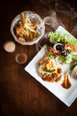 Grilled chicken steak with lettuce salad cherry tomatoes mushrooms herbs  on  white plate and wooden background. Traditional cuisine. Grill kitchen.