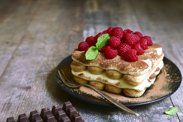 Homemade tiramisu with raspberry on a black plate.