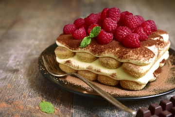 Homemade tiramisu with raspberry on a black plate.