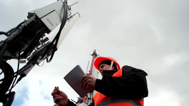 employees mobile Company, cellular, an engineer working with the antennas and transmitters on the tower, records data on a background of gray sky, a man dressed in uniform and hel
