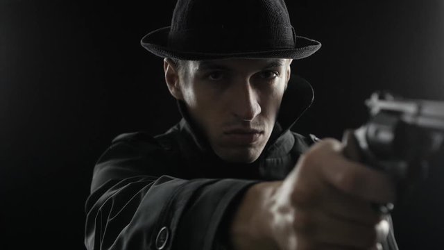 Portrait of a gangster in a hat and a black cloak threatens weapon