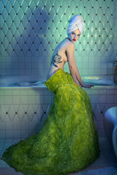 Woman in green skirt sitting on bath with tattooed back 