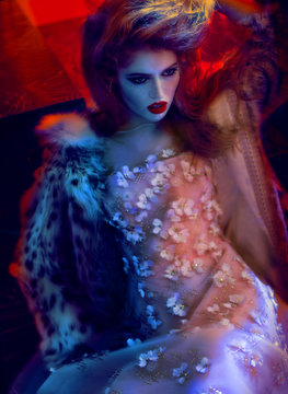 Woman in shimmer dress and fur coat reclining, portrait 