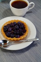 Tasty tart with blueberry and hot black tea in a white cup