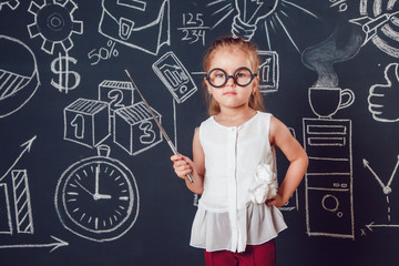 The little smart girl in glasses holding a pointer on dark background with business or school picture