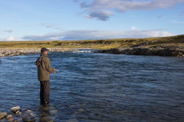 Fisherman fishing in the shallows of a wild mountain river. Fishing on Polar Ural Mountains.